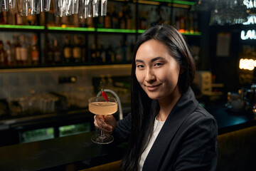 Asian woman celebrating her success drinking tasty vanilla-sweet cocktail