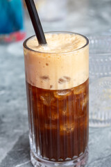 A close-up of a chilled cold brew coffee topped with foam and served in a tall glass with a straw, perfect for a hot day.