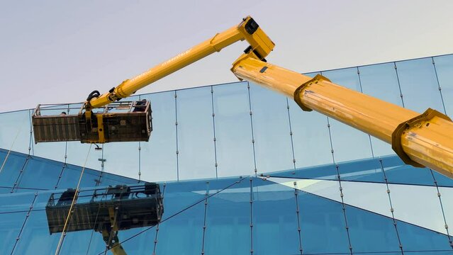 Cleaner worker using a cherry picker to clean a glas facade of a contemporary office building