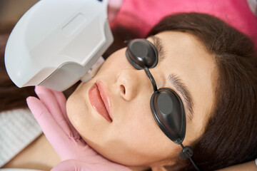Female patient getting IPL photofacial carried out by esthetician