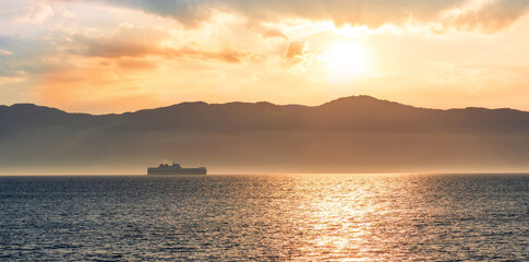 tropical seascape of sailing kargo tanker ship in sea with beautiful sunset and mountains on background