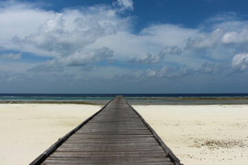 A long jetty, pier at the white sand beach coast of a tropical Maratua island in East Kalimantan on a bright sunny day with blue sky