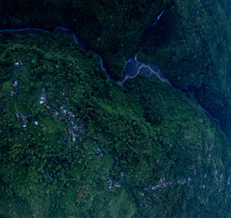Aerial view Kabut Pelangi Waterfall in East Java. The waterfall crashes down into the amphitheater below, which is covered in lush green plants. Above is the residence of the villagers.