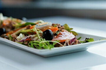 Salad with cabbage, cucumber, egg, onion, tuna and olive oil on a white saucer on a white background