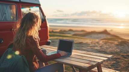 A female working on laptop by vintage camper van at sea beach in summer vacation