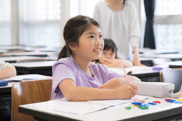 教室で授業中に勉強をし鉛筆を持つ小学生の女の子見上げて黒板を写す