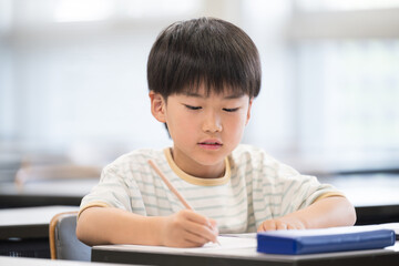 教室で授業中に勉強をし鉛筆を持つ小学生の男の子