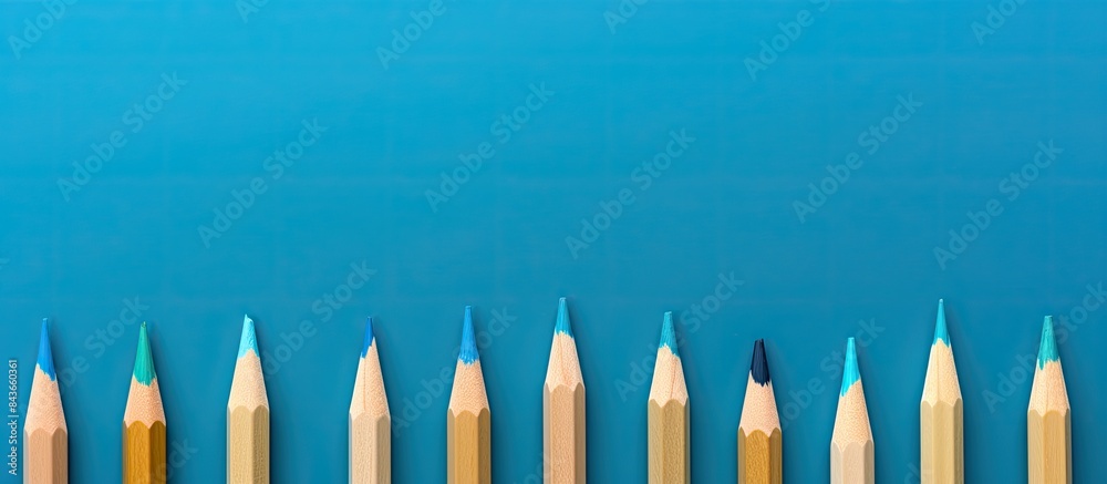 Poster Wooden colored pencils neatly arranged in a row on a blue background seen from a top down perspective with ample space for text or images