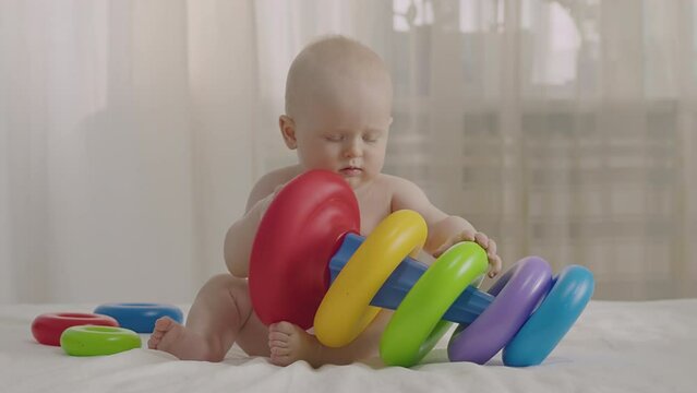 Infant interact with vibrant stackable toy, fun baby boy play with colorful rings on bed, focus and engage. Development and learn through play and cognitive growth. Early education, child care and toy