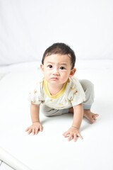 Fototapeta premium A baby with a sad expression is crawling on a white surface, dressed in light-colored clothes with animal prints. The baby looks curious yet slightly upset, highlighting innocence and emotion.