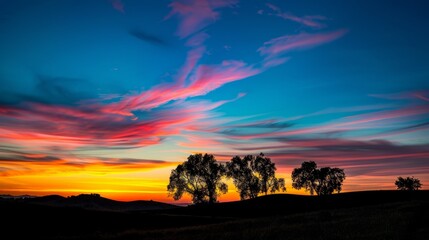 A low angle shot captures a dramatic sunset over a peaceful countryside, with colorful hues painting the sky in vibrant shades of pink, orange, and blue