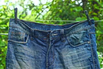 single blue with pockets men's stylish with iron button and zipper fashionable old worn jeans hanging in a green garden during the day