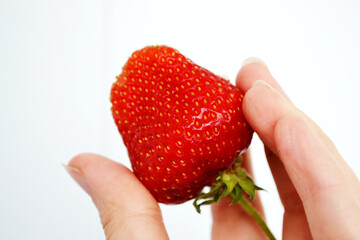 hand is holding a fresh, ripe strawberry. The strawberry is vibrant red in color, with small seeds visible on its surface.  image captures the essence of summer with a delicious strawberry 
