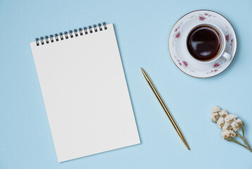 Empty notebook with gold pen, cup of coffee and flower on blue background from above. Space for text