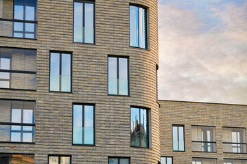 Modern residential building with large windows and clinker brick facade against susnet sky. Clinker brick facade and floor-to-ceiling glass windows.
