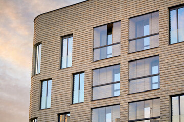 Modern residential building with large windows and clinker brick facade against susnet sky. Clinker brick facade and floor-to-ceiling glass windows.