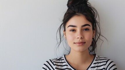 Fototapeta premium Shy and positive girl in striped shirt looking attentively at the camera while standing on a white backdrop