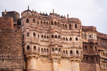Obraz premium majestic stone walls of mehrangarh fort with window arches in jodhpur sitting on top of hill surrounded by monsoon clouds with birds flying around this landmark of rajput warrior history