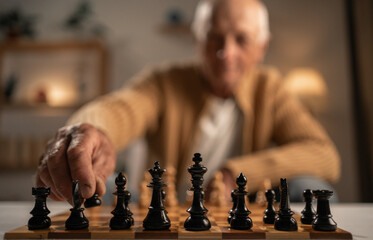 close-up of an elderly man playing chess, chessboard with pieces in the foreground and blurred background. Hobby and leisure
