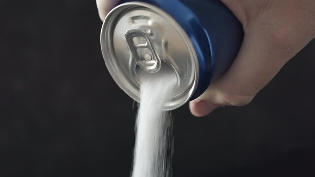 Sugar pours from opened can, closeup on artificial sweetener flowing from the soda can.