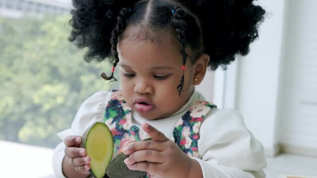 Little cute black girl picks up avokado one half to connect with the other half that is holding.