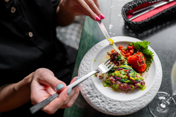 Close-up of a person’s hands using utensils to enjoy a gourmet dish, showcasing the vibrant colors and textures of fine dining