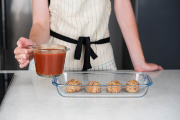 Female chef in an apron preparing meat or cutlets patties with rice, baking them in a dish with tomato sauce. Home cooking, traditional recipes, and culinary preparation.
