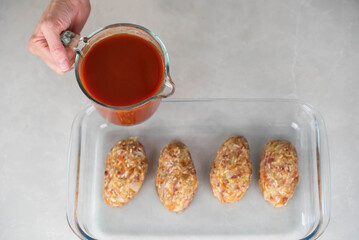Female chef in an apron preparing meat or cutlets patties with rice, baking them in a dish with tomato sauce. Home cooking, traditional recipes, and culinary preparation.
