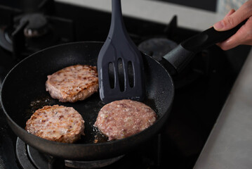 Meatballs or small meat patties cutlets sizzling in oil while frying in a pan on the stove. Concept of home cooking, traditional recipes, and culinary preparation