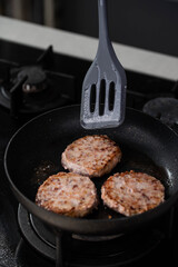 Meatballs or small meat patties cutlets sizzling in oil while frying in a pan on the stove. Concept of home cooking, traditional recipes, and culinary preparation