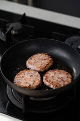Meatballs or small meat patties cutlets sizzling in oil while frying in a pan on the stove. Concept of home cooking, traditional recipes, and culinary preparation