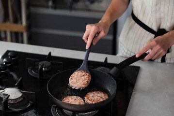 Meatballs or small meat patties cutlets sizzling in oil while frying in a pan on the stove. Concept of home cooking, traditional recipes, and culinary preparation