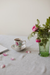 Moody summer still life. Table composition with cup of coffee, tea and beautiful floral bouquet with pink roses