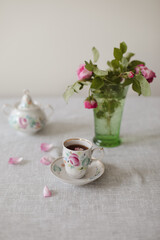Moody summer still life. Table composition with cup of coffee, tea and beautiful floral bouquet with pink roses