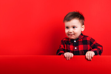Baby in red flannel shirt on red background. Child's emotions, template, blank, looking at text, copy space.