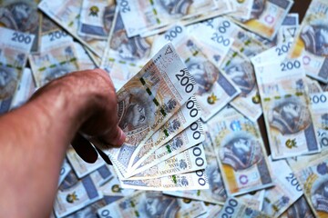 Trzymane w dłoni pieniądze o wartości 1000 złotych. W tle widać inne banknoty o nominale 200 złotych. Dokonywanie transakcji z pomocą gotówki.