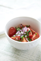 Simple salad with cherry tomatoes, red onion and fresh herbs. Bright wooden background.	