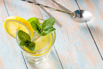 Lemonade Ice Drink in Glass with Mint and Lemon on Pastel Wooden Surface
