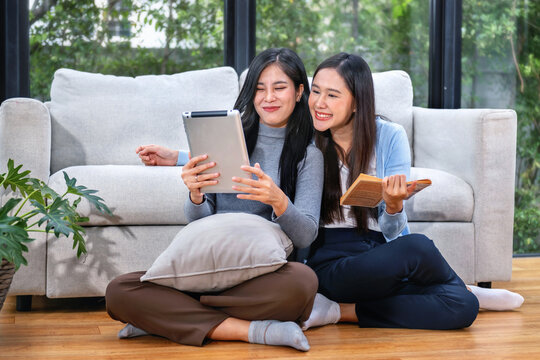 Two women sitting on the floor, one holding a tablet and the other a book