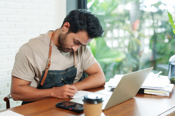 Close-up of face of handsome bearded Indian man working with laptop. Businessman. Coffee shop. Small family business. Sitting and working is stressful. Think a lot about store's income and expenses.