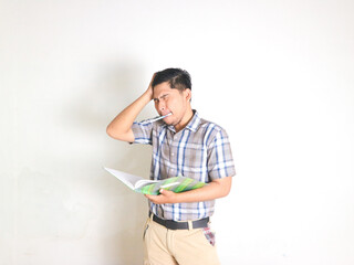 Asian man wearing a plaid shirt holding his head because of stress and frustration when looking at a report in the book he was holding