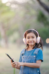 Little girl using smartphone and headphones in nature and having fun.