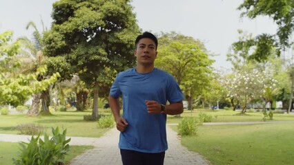 Tracking shot of motivated Asian man running in local park on Sunday morning alone