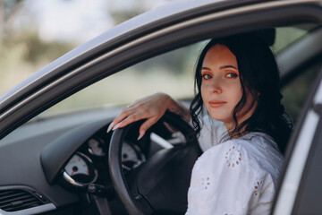 Naklejka premium woman with black hair sits in the driver’s seat of a grey sedan car, facing the camera. The photo is a portrait, capturing her serene expression and the interior details of the vehicle