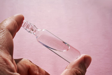 Ampoule for injection with medicines on a pink background in hand.