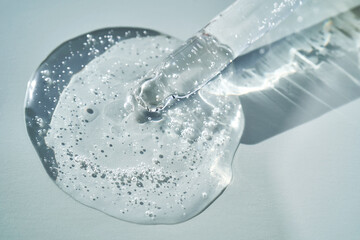 Pipette with serum shimmering in the sun on a blue background.