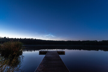 Noctilucent clouds over the forest lake in Latvia on June night