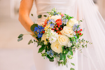 A bride holds her wedding bouquet, which is an assortment of different roses and colors.