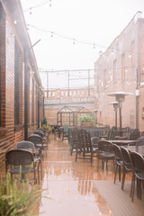 Drizzly rainy day on a restaurant patio with wet chairs and black tables. 