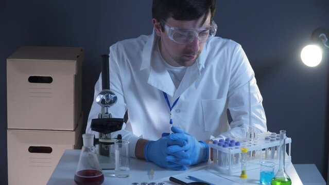 Man, tired medical worker in laboratory sitting at his workplace and pensively looking at one point. Tired male scientist with microscope working in laboratory. Biochemist, pathologist stumped at work